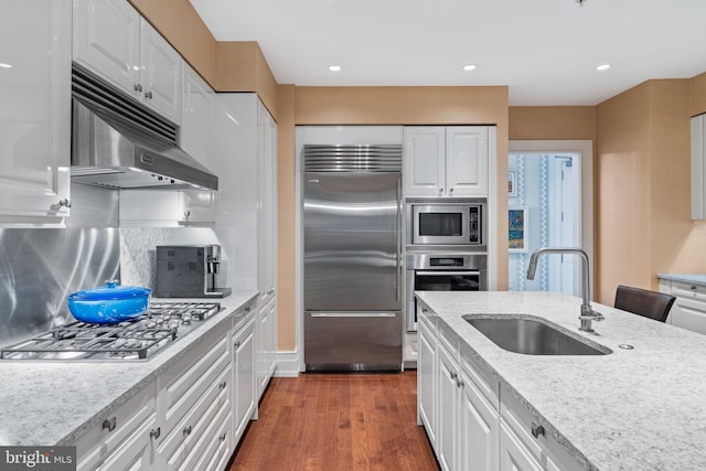 kitchen with light stone countertops, dark hardwood / wood-style flooring, sink, built in appliances, and white cabinets