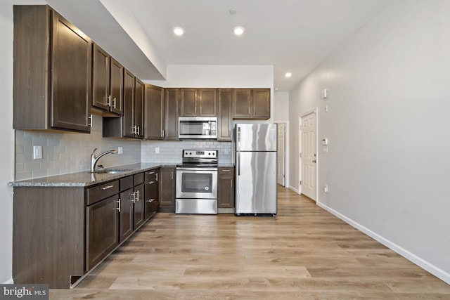 kitchen featuring stone countertops, sink, appliances with stainless steel finishes, dark brown cabinets, and light hardwood / wood-style flooring