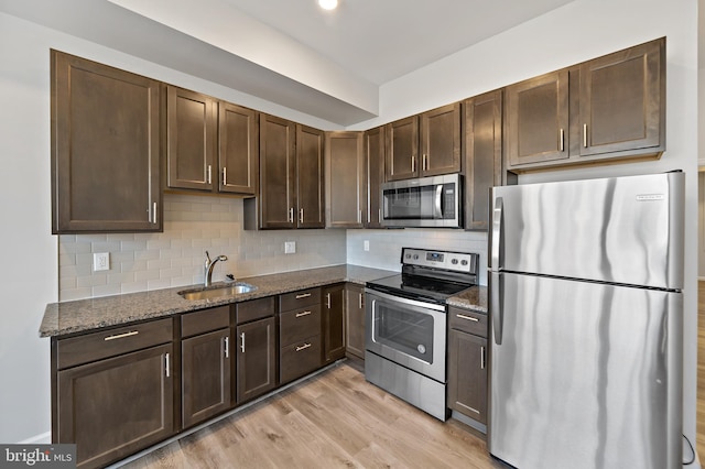 kitchen featuring tasteful backsplash, light wood-type flooring, appliances with stainless steel finishes, sink, and dark stone countertops