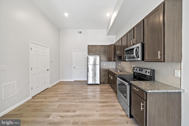 kitchen with light hardwood / wood-style floors, sink, appliances with stainless steel finishes, light stone countertops, and dark brown cabinets