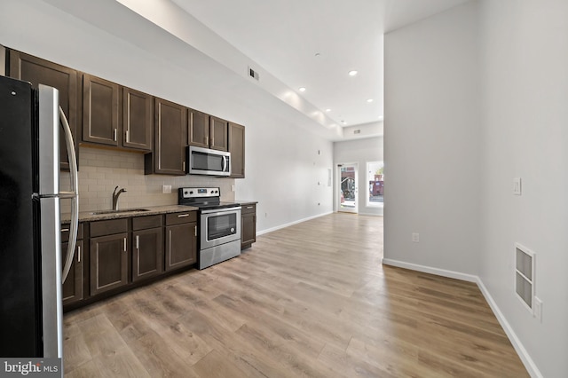 kitchen featuring stainless steel appliances, light wood-type flooring, dark brown cabinetry, decorative backsplash, and sink