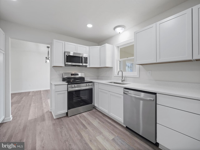 kitchen featuring appliances with stainless steel finishes, light hardwood / wood-style flooring, white cabinetry, and sink