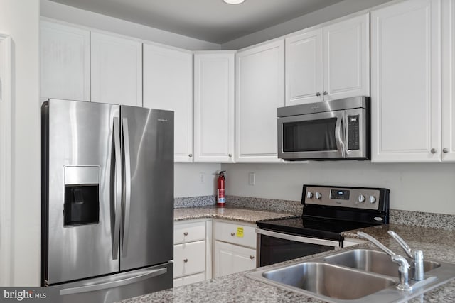 kitchen with stainless steel appliances, white cabinets, sink, and light stone counters