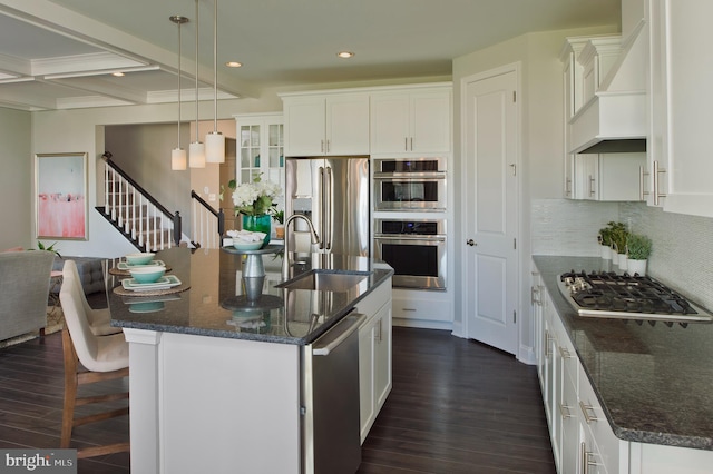 kitchen featuring dark hardwood / wood-style flooring, a center island with sink, white cabinets, custom range hood, and appliances with stainless steel finishes