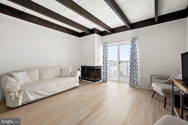 living room featuring a wall unit AC, light hardwood / wood-style floors, and beam ceiling