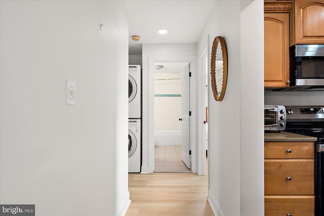 laundry area with light hardwood / wood-style floors and stacked washer / drying machine