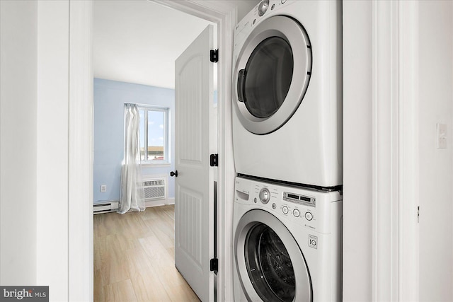 laundry room featuring a wall unit AC, baseboard heating, stacked washer / dryer, and light wood-type flooring