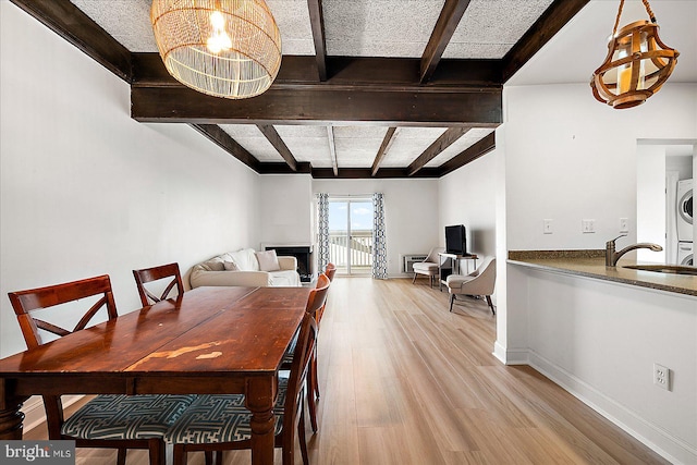 dining room featuring sink, beam ceiling, an inviting chandelier, light hardwood / wood-style flooring, and stacked washer and dryer