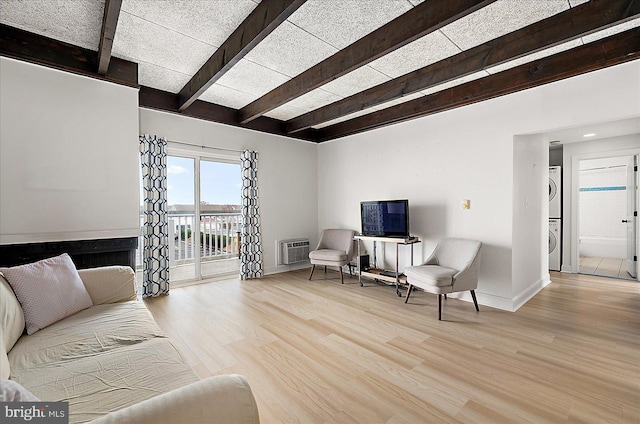 living room with stacked washer and clothes dryer, a wall mounted AC, light hardwood / wood-style floors, and beamed ceiling