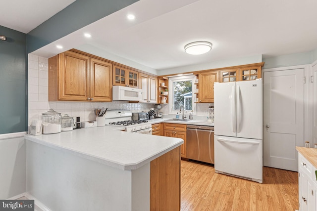 kitchen featuring sink, kitchen peninsula, white appliances, decorative backsplash, and light wood-type flooring