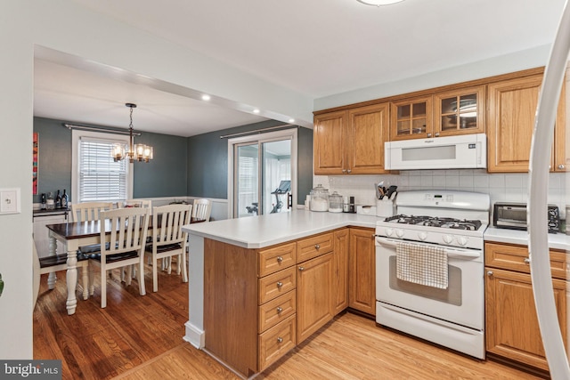 kitchen featuring light wood-type flooring, white appliances, decorative light fixtures, and kitchen peninsula