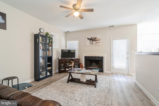 living room featuring a tile fireplace, ceiling fan, and light hardwood / wood-style flooring