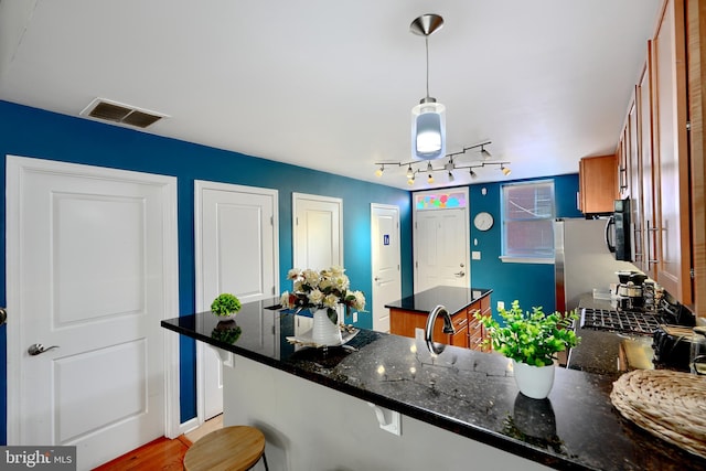 kitchen with a kitchen bar, light hardwood / wood-style floors, kitchen peninsula, pendant lighting, and dark stone countertops