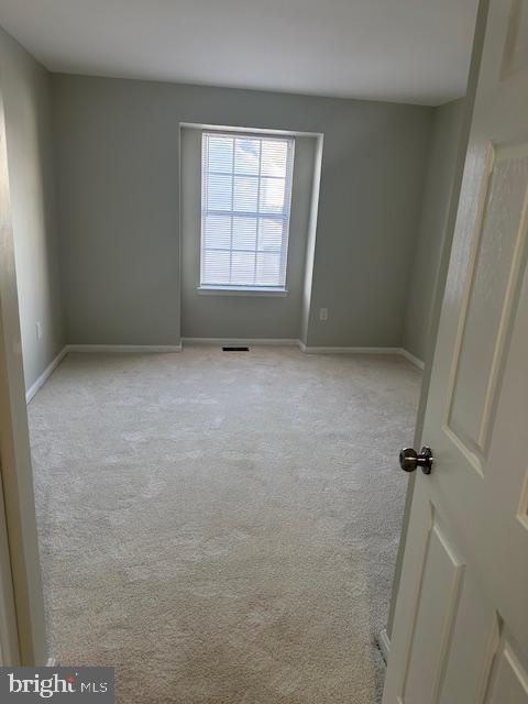 spare room featuring light carpet and baseboards