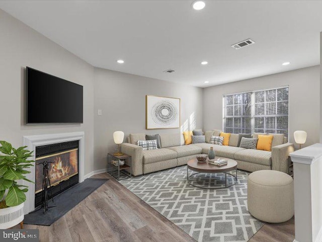 living room featuring a glass covered fireplace, wood finished floors, visible vents, and recessed lighting