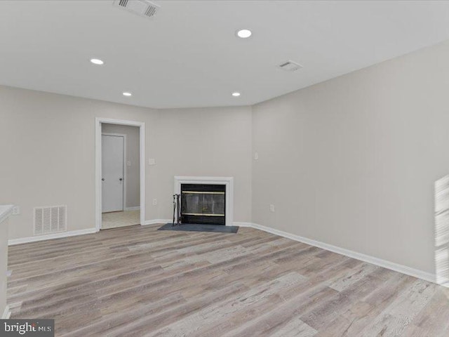 unfurnished living room with a fireplace with flush hearth, visible vents, and wood finished floors