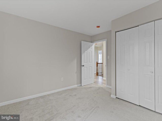 unfurnished bedroom featuring a closet, light carpet, and baseboards