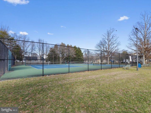 view of tennis court featuring fence and a yard