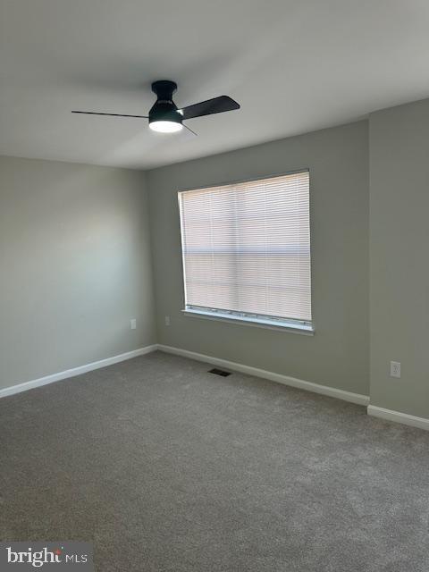 spare room with a ceiling fan, carpet flooring, visible vents, and baseboards