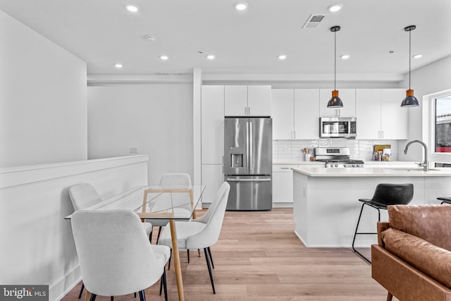 kitchen with sink, pendant lighting, stainless steel appliances, light hardwood / wood-style floors, and white cabinets