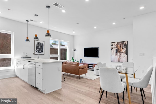 kitchen with decorative light fixtures, white cabinetry, dishwasher, sink, and light hardwood / wood-style flooring