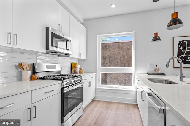 kitchen with tasteful backsplash, white cabinetry, sink, hanging light fixtures, and stainless steel appliances