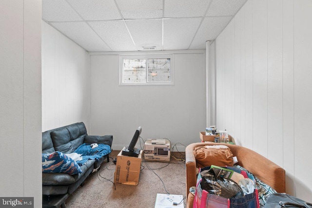 living area featuring carpet flooring, wood walls, and a drop ceiling