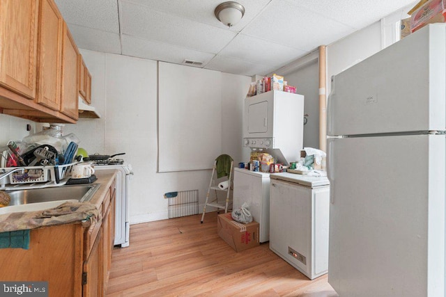 kitchen with white refrigerator, a paneled ceiling, range with gas cooktop, stacked washer and dryer, and light wood-type flooring