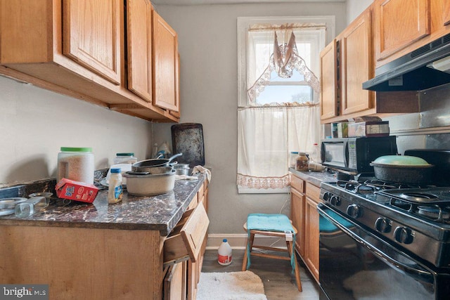 kitchen with dark stone counters, black gas range oven, extractor fan, and wood-type flooring