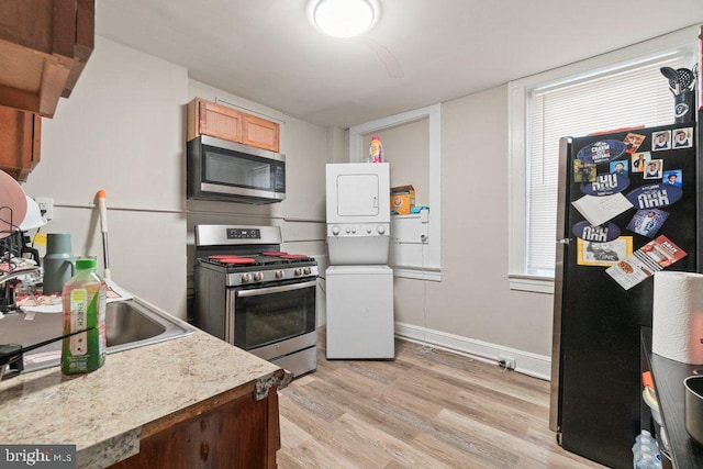 kitchen featuring stainless steel appliances, stacked washing maching and dryer, sink, and light wood-type flooring