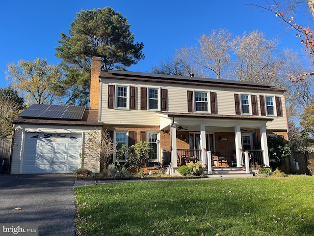 colonial-style house with a garage, covered porch, a front yard, and solar panels