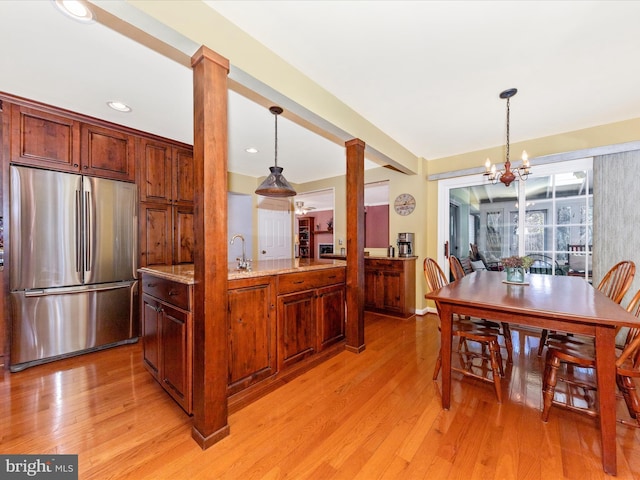 kitchen with hanging light fixtures, light stone countertops, stainless steel refrigerator, and ornate columns