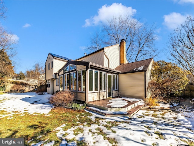 snow covered rear of property featuring a sunroom