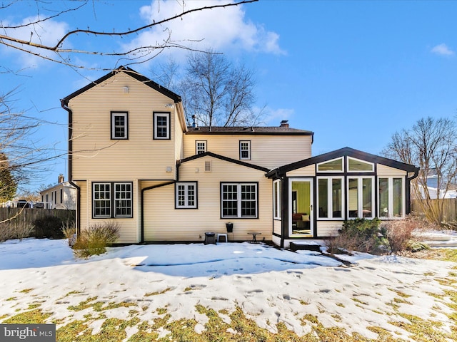 snow covered rear of property with a sunroom