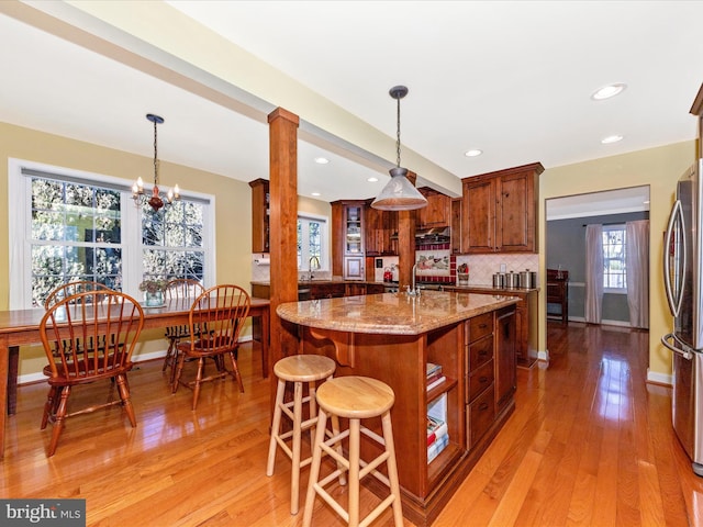 kitchen with light wood-type flooring, stainless steel fridge, light stone counters, and decorative light fixtures