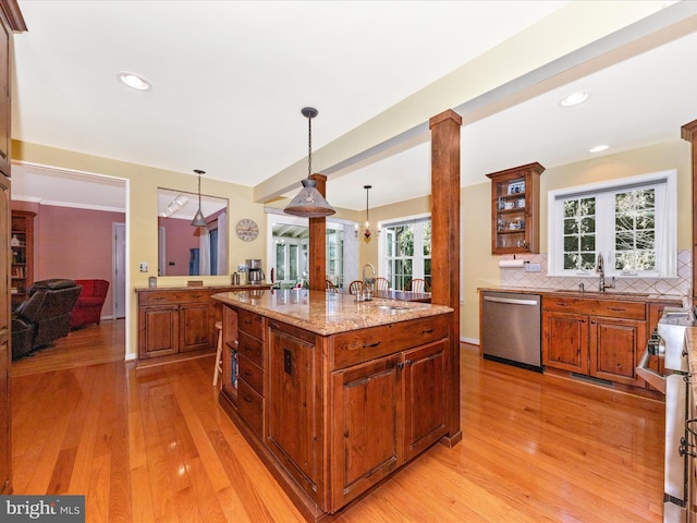 kitchen with sink, decorative light fixtures, appliances with stainless steel finishes, a kitchen island, and light stone countertops