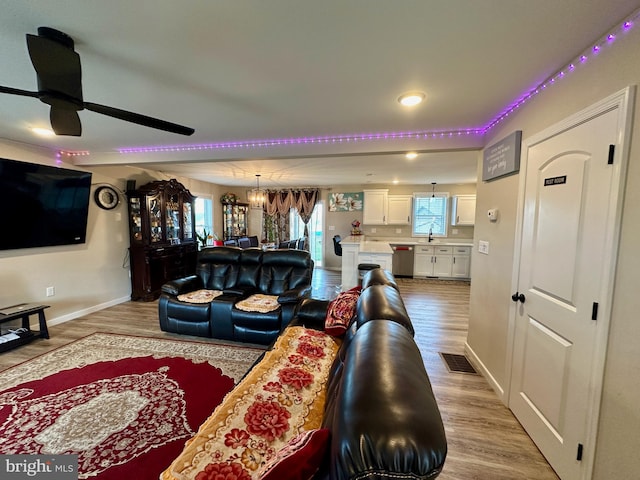 living room with ceiling fan with notable chandelier, light wood-type flooring, and sink