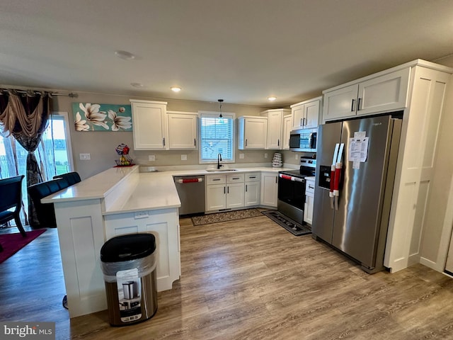 kitchen with pendant lighting, sink, light hardwood / wood-style flooring, kitchen peninsula, and stainless steel appliances