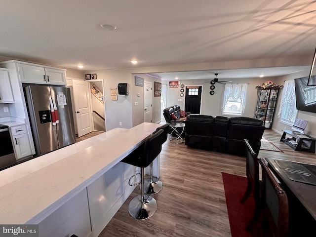 kitchen with dark wood-type flooring, light stone counters, stainless steel refrigerator with ice dispenser, a kitchen bar, and white cabinets