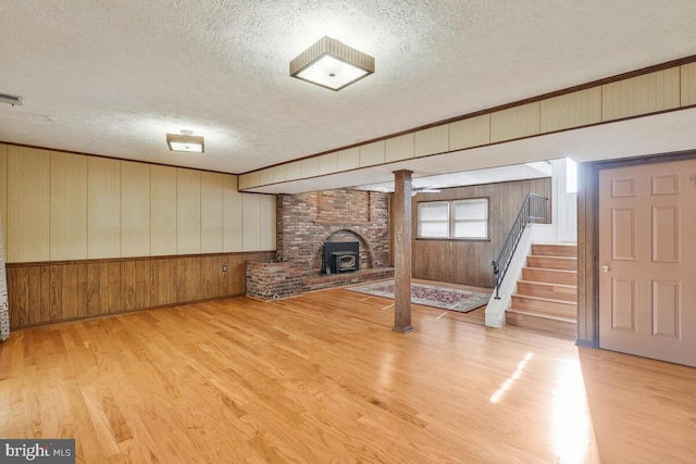 basement featuring a wood stove, a textured ceiling, light hardwood / wood-style flooring, and wood walls