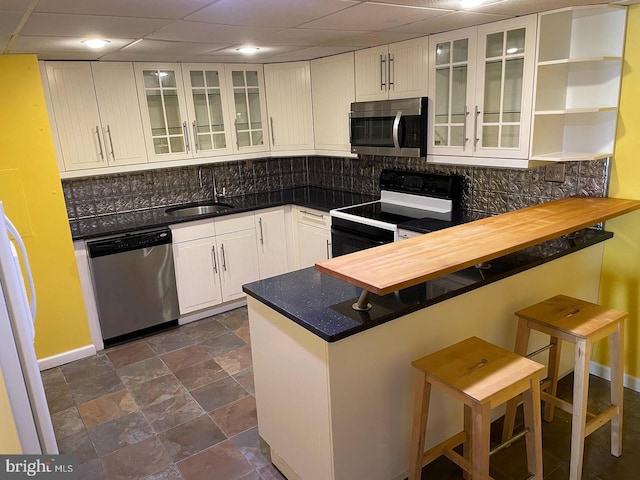 kitchen with kitchen peninsula, decorative backsplash, a breakfast bar, and appliances with stainless steel finishes