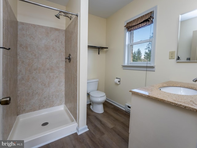 bathroom featuring wood-type flooring, a tile shower, vanity, a baseboard radiator, and toilet