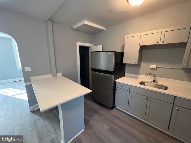 kitchen with kitchen peninsula, dark hardwood / wood-style flooring, sink, and stainless steel refrigerator