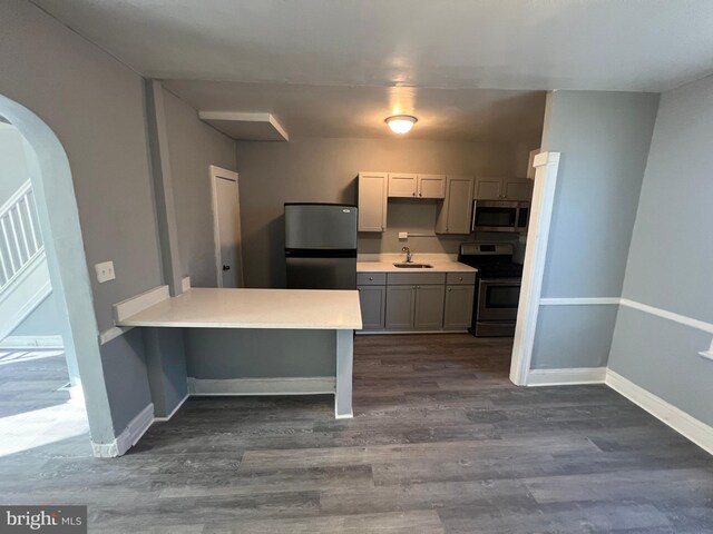 kitchen featuring dark wood-type flooring, kitchen peninsula, sink, gray cabinets, and appliances with stainless steel finishes