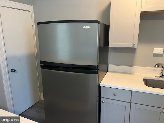 kitchen featuring stainless steel refrigerator, dark hardwood / wood-style floors, sink, and white cabinetry