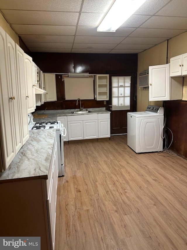 kitchen with white cabinetry, sink, white gas stove, light hardwood / wood-style flooring, and washer / dryer