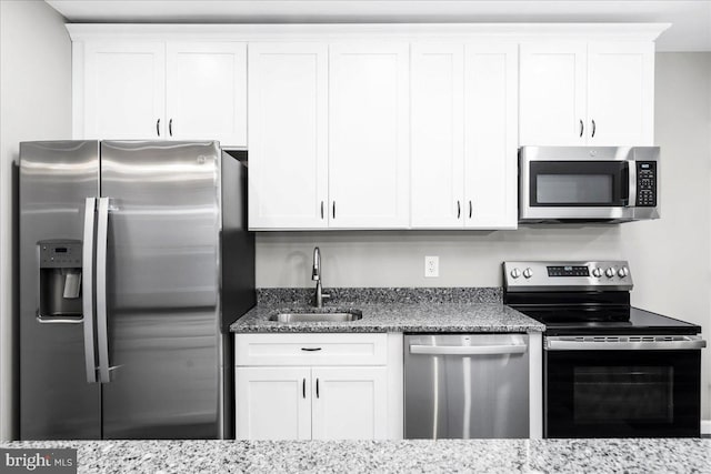 kitchen with light stone countertops, white cabinetry, sink, and stainless steel appliances