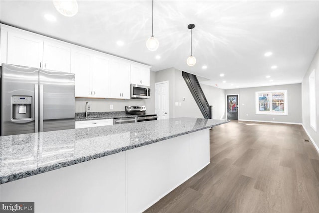 kitchen with appliances with stainless steel finishes, light stone counters, dark wood-type flooring, pendant lighting, and white cabinetry