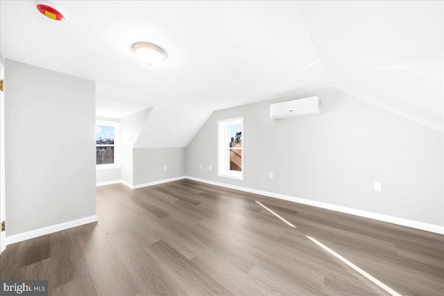 bonus room with vaulted ceiling, a wall unit AC, and dark wood-type flooring