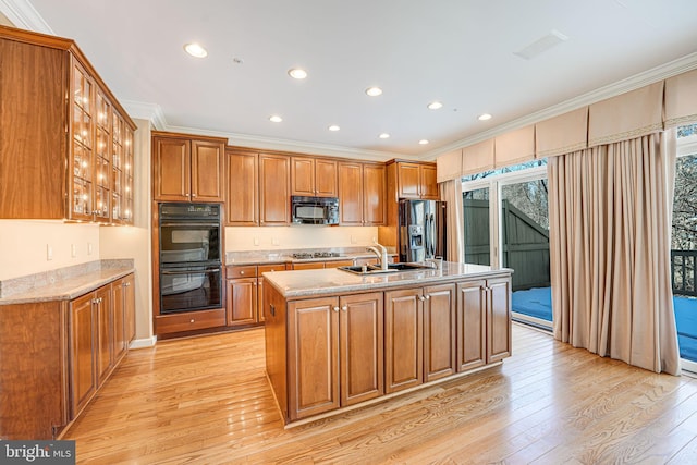 kitchen featuring sink, black appliances, a healthy amount of sunlight, and an island with sink